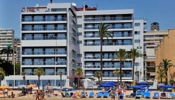 Sol Costablanca Adults-only hotel. Gay-friendly hotel on the beach. People enjoy the beach in front of the hotel. Palm trees.