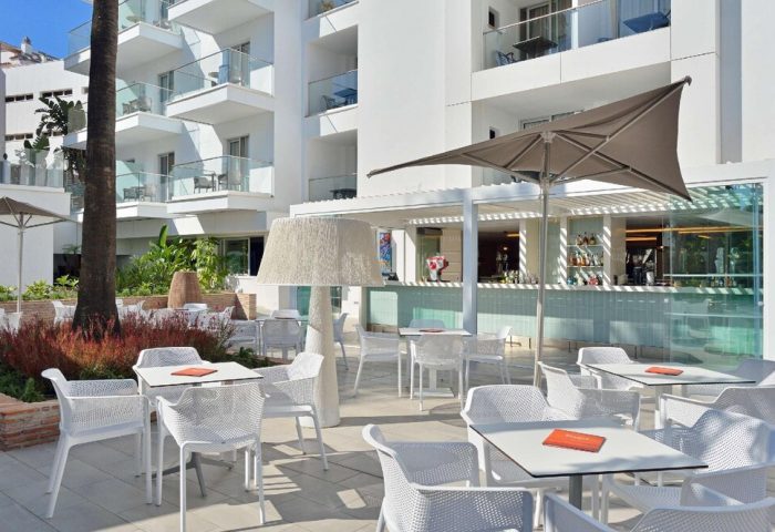 Sol Torremolinos Don Pablo gay-friendly hotel outdoor bar area. White tables and chairs under umbrellas. Modern, bright, and inviting space.