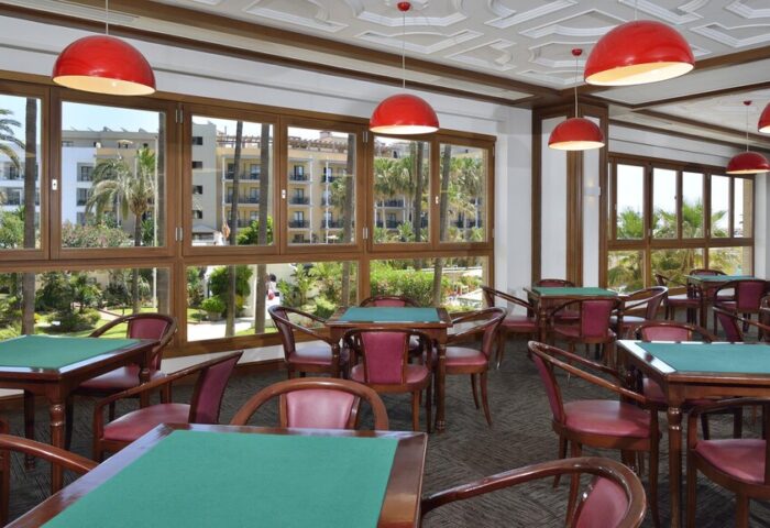Sol Torremolinos Don Pablo Hotel's card room. Tables with green tops, red chairs, and red pendant lights. Gay-friendly travel destination.