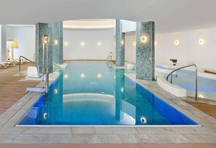 Sol Torremolinos Don Pablo gay-friendly hotel indoor pool. Modern design with blue water, columns, and lounge chairs for a relaxing vacation.