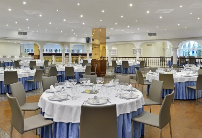 Sol Torremolinos Don Pablo gay-friendly hotel dining room. Round tables with white tablecloths and blue skirts, set for a meal.