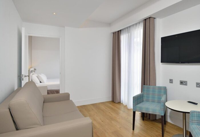 Sol Torremolinos Don Pedro gay-friendly hotel room. Seating area with sofa, TV, and view into bedroom. Modern, clean design.
