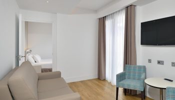 Sol Torremolinos Don Pedro gay-friendly hotel room. Seating area with sofa, TV, and view into bedroom. Modern, clean design.