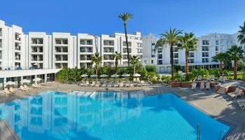 Sol Torremolinos Don Pedro hotel view. Gay-friendly hotel with pool, palm trees, and lounge chairs. Ideal for gay travel and relaxation.