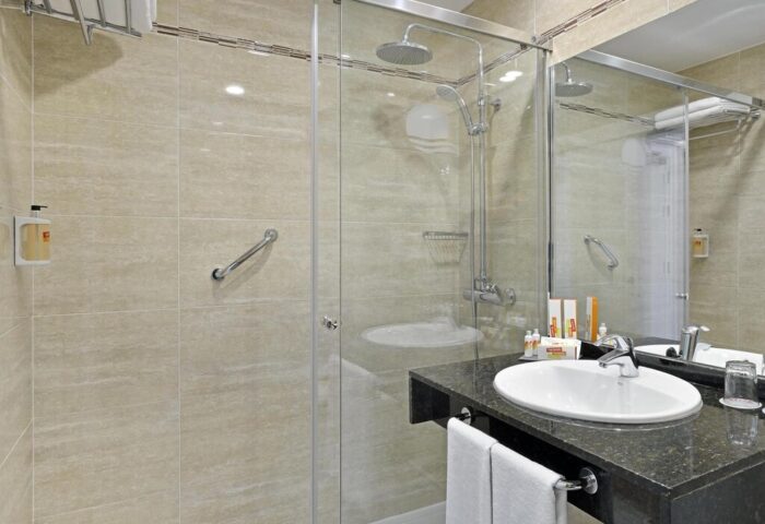 Bathroom at Sol Torremolinos - Don Pedro, a gay-friendly hotel. Features a glass shower, sink with black granite countertop, and accessible grab bar.