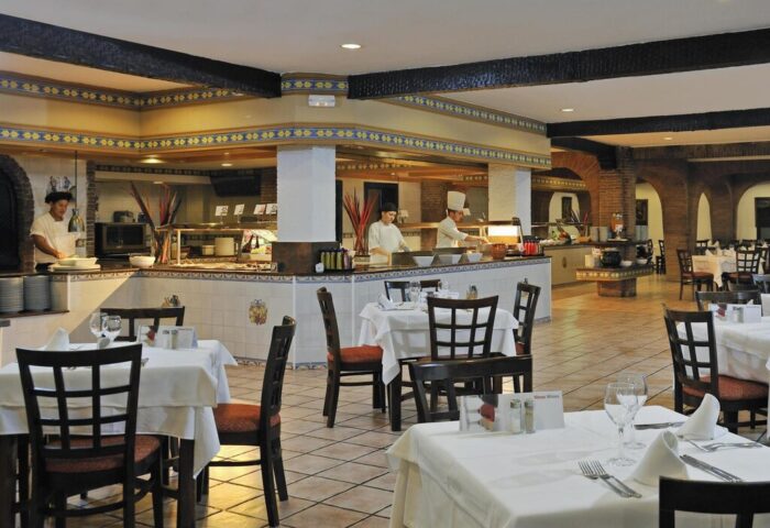 Dining area at Sol Torremolinos Don Pedro, a gay-friendly hotel. Tables with white linens, chefs at buffet. Tile flooring, arched brick details.