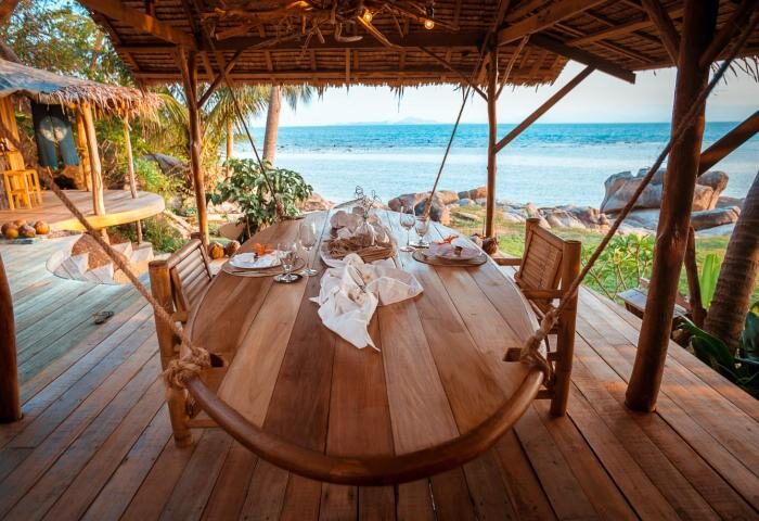 Somewhere Only We Know gay-friendly hotel: Beachside dining at a luxury resort. Wooden table set for a meal overlooking the ocean.