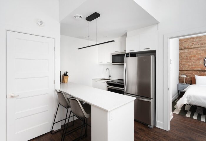 Sonder Gare Saint Denis gay-friendly hotel room. Modern kitchen with bar seating, stainless steel fridge, and view into the bedroom.