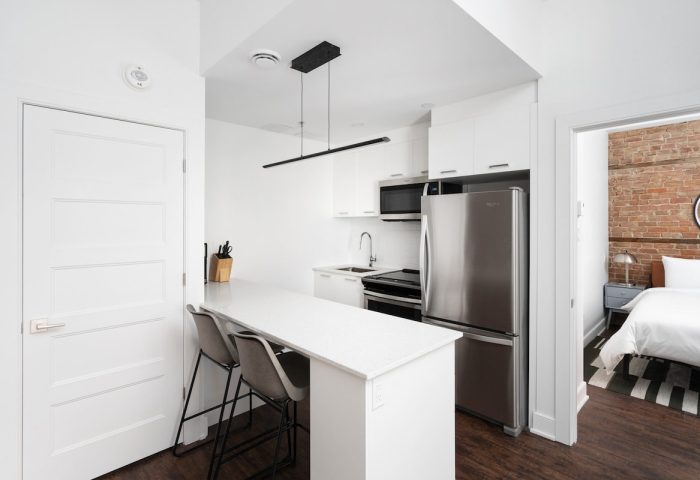 Sonder Gare Saint Denis gay-friendly hotel room. Modern kitchen with bar seating, stainless steel fridge, and view into the bedroom.