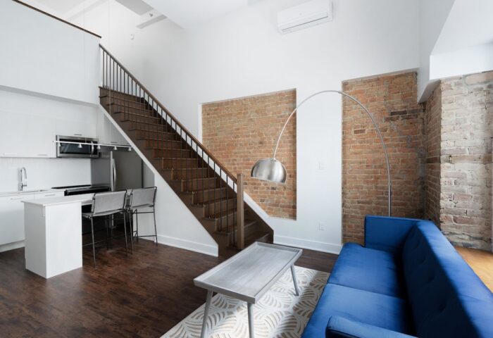 Sonder Gare Saint Denis gay-friendly hotel room. Modern interior with kitchen, stairs, exposed brick, blue couch, and stylish decor.