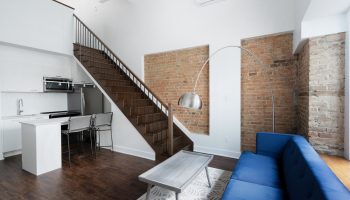 Sonder Gare Saint Denis gay-friendly hotel room. Modern interior with kitchen, stairs, exposed brick, blue couch, and stylish decor.