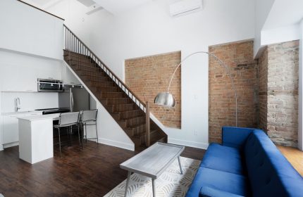 Sonder Gare Saint Denis gay-friendly hotel room. Modern interior with kitchen, stairs, exposed brick, blue couch, and stylish decor.