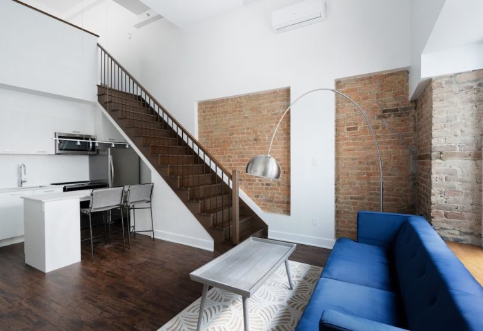 Sonder Gare Saint Denis gay-friendly hotel room. Modern interior with kitchen, stairs, exposed brick, blue couch, and stylish decor.