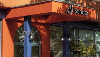 Sonder The Sunset, a gay-friendly hotel. The entrance boasts vibrant orange & blue colors, plants, and the Sonder logo for gay travelers.