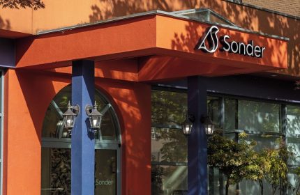 Sonder The Sunset, a gay-friendly hotel. The entrance boasts vibrant orange & blue colors, plants, and the Sonder logo for gay travelers.