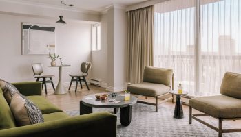 Sonder The Sunset gay-friendly hotel room. Modern interior with green sofa, chairs, table, and city view. Ideal for gay travel.