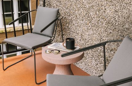 Sonder The Sunset hotel's gay-friendly patio. Two chairs flank a table with coffee, glasses, and a newspaper. Relaxing travel vibe.