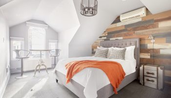 Sonder The Wellesley gay-friendly hotel room. Attic suite with bed, orange throw, wood accent wall, and table with stools by window.