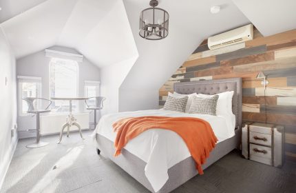 Sonder The Wellesley gay-friendly hotel room. Attic suite with bed, orange throw, wood accent wall, and table with stools by window.