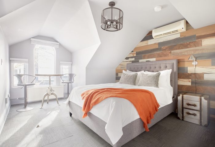 Sonder The Wellesley gay-friendly hotel room. Attic suite with bed, orange throw, wood accent wall, and table with stools by window.