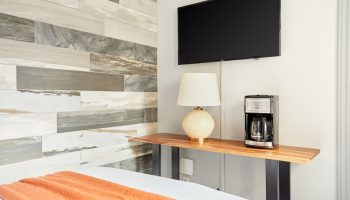 Sonder The Wellesley gay-friendly hotel room detail: TV, lamp, coffee maker on a wooden shelf. Modern design with wood-style wall tiles.