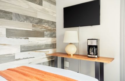 Sonder The Wellesley gay-friendly hotel room detail: TV, lamp, coffee maker on a wooden shelf. Modern design with wood-style wall tiles.