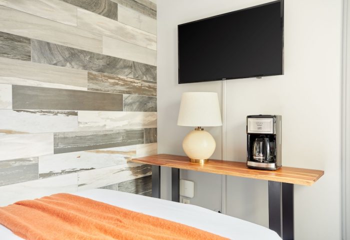 Sonder The Wellesley gay-friendly hotel room detail: TV, lamp, coffee maker on a wooden shelf. Modern design with wood-style wall tiles.