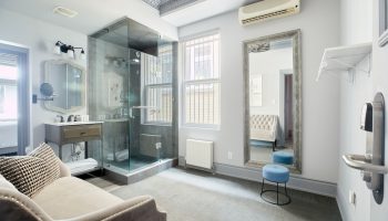 Sonder The Wellesley gay-friendly hotel bathroom. Glass shower, vanity, large mirror, stool, and stylish decor. Gay travel lodging.