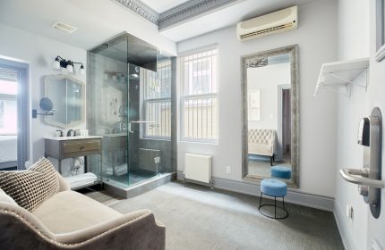 Sonder The Wellesley gay-friendly hotel bathroom. Glass shower, vanity, large mirror, stool, and stylish decor. Gay travel lodging.