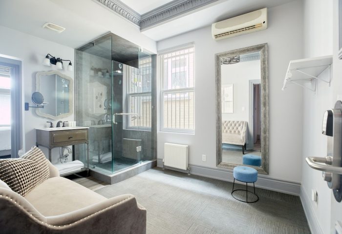 Sonder The Wellesley gay-friendly hotel bathroom. Glass shower, vanity, large mirror, stool, and stylish decor. Gay travel lodging.