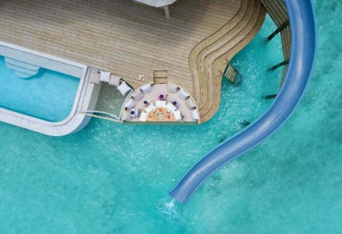 Aerial view of Soneva Fushi, a gay-friendly hotel. Features include a pool, dining area, and a water slide into the turquoise ocean.