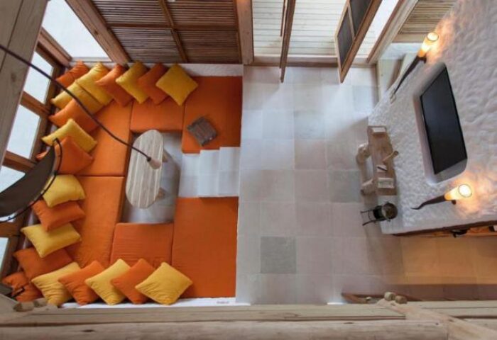 Soneva Fushi gay-friendly hotel: Top-down view of a luxury villa interior with orange cushions, wooden table, and TV. Ideal for gay travel.