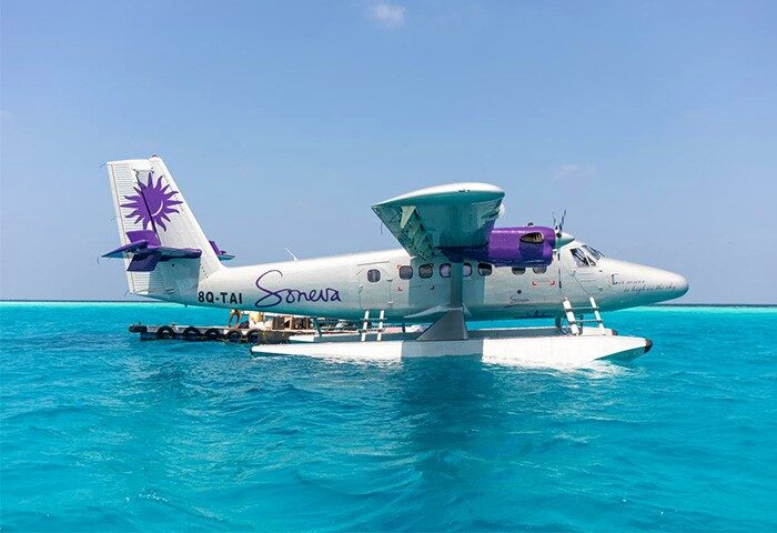 Soneva Fushi seaplane in Maldives. Gay-friendly hotel offers scenic flights. Turquoise water surrounds the plane. Luxury travel experience.