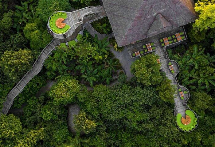 Aerial view of Soneva Fushi, a gay-friendly hotel. Wooden walkways connect treetop dining areas in lush greenery. Perfect for gay travel.