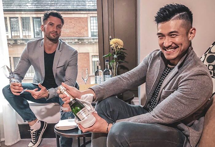 Two gay men with champagne at South Place Hotel, a gay-friendly, pet-friendly hotel. Celebrating with drinks in a hotel room.