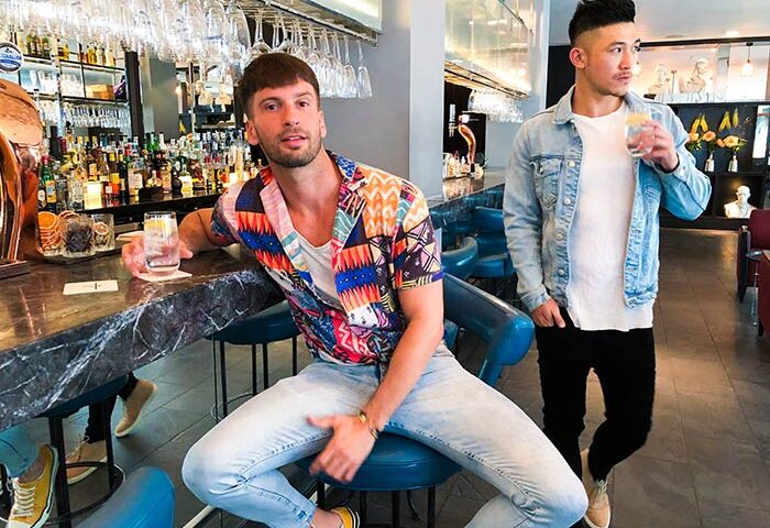 Two gay men at South Place Hotel bar. One sits at the bar, the other stands. Gay-friendly, pet-friendly hotel.