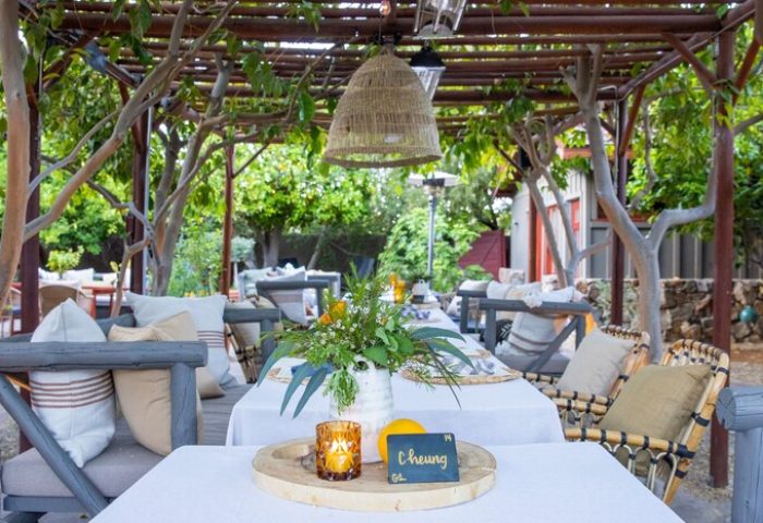 Sparrows Lodge, a gay-friendly hotel. Outdoor dining area with tables set for a meal. The tables are covered with white tablecloths. Wicker chairs around.