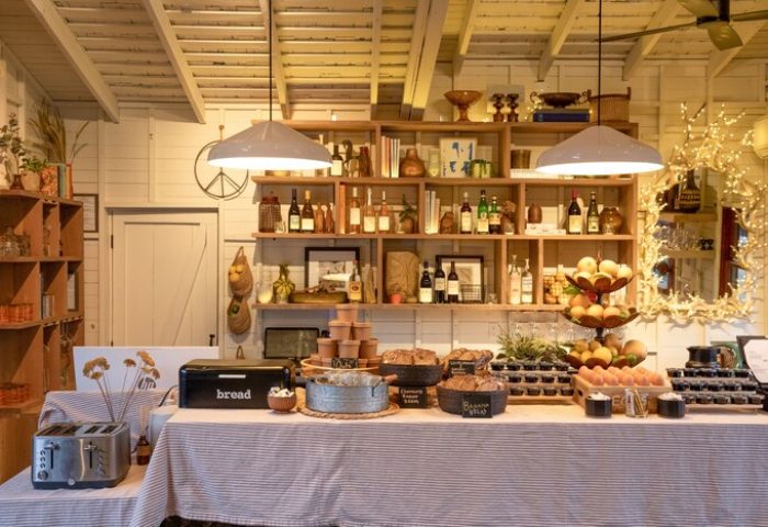 Breakfast bar at Sparrows Lodge, a gay-friendly hotel. Rustic decor with baked goods, fruit, and shelves stocked with wine and decorative items.