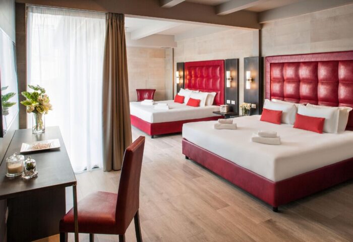 Spice Hotel Milano gay-friendly room. Red headboards, white linens, towels. Desk with flowers. Modern design, comfortable for gay travelers.