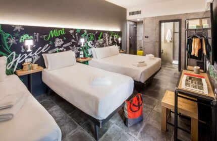 Spice Hotel Milano gay-friendly room. Three beds, desk, and bathroom. Modern design with a chalkboard-style headboard. Gay travel lodging.
