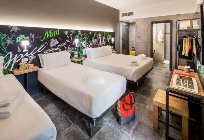 Spice Hotel Milano gay-friendly room. Three beds, desk, and bathroom. Modern design with a chalkboard-style headboard. Gay travel lodging.