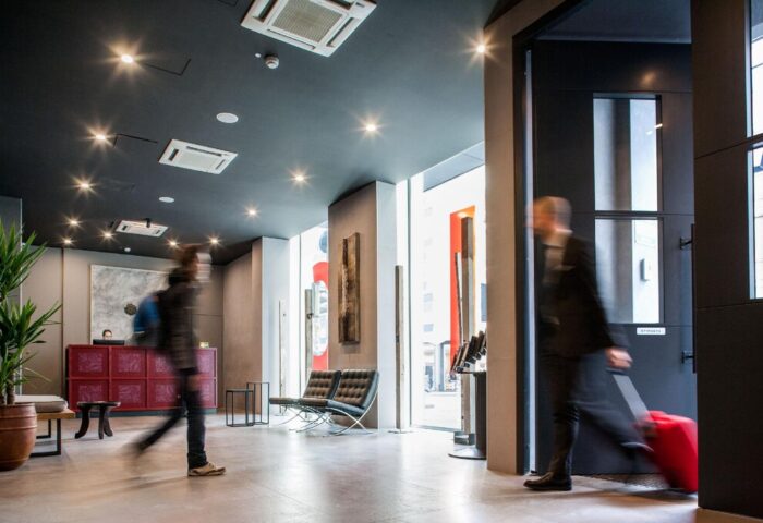 Spice Hotel Milano lobby. Gay-friendly hotel with modern design. Travelers arrive with luggage. Welcoming space for gay men's travel.