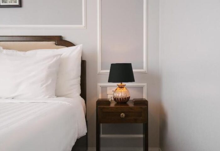 Bedroom detail at Spring Flower Hotel, a gay-friendly hotel. Nightstand with lamp next to bed with white linens. Interior design.