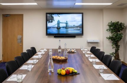 Conference room at St Giles London Hotel. Long table with fruit, water, and snacks. TV shows Tower Bridge. Gay-friendly hotel in London.