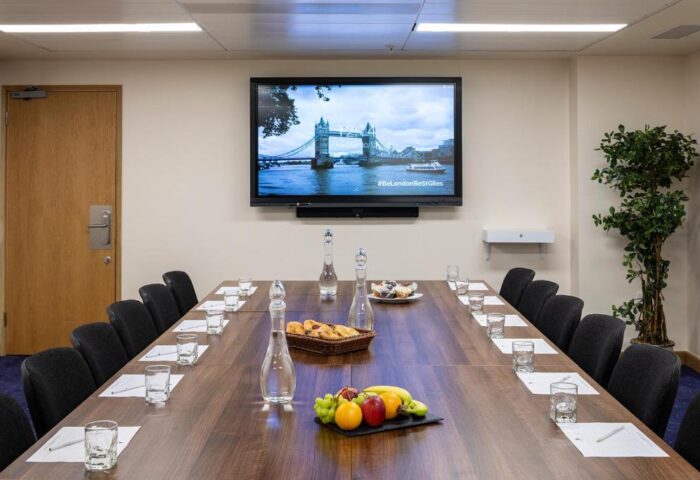 Conference room at St Giles London Hotel. Long table with fruit, water, and snacks. TV shows Tower Bridge. Gay-friendly hotel in London.