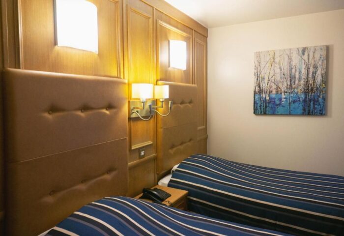 St Giles London hotel room with twin beds, striped bedding, wood paneling, and wall art. A gay-friendly, pet-friendly hotel.