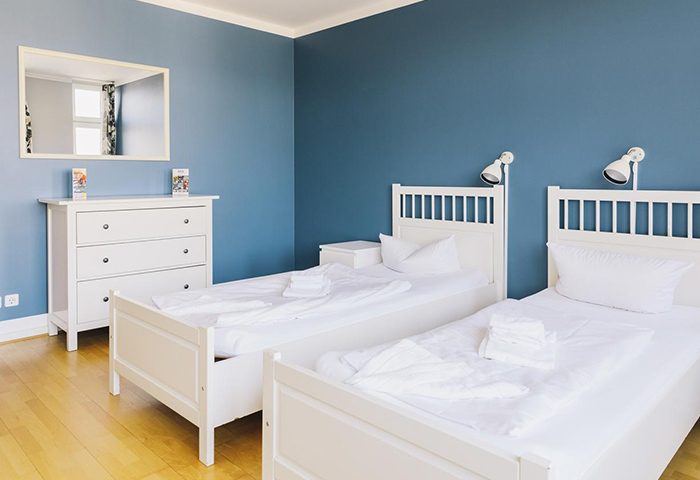 St. Christopher's Hostel Berlin: Gay-friendly hotel room with two beds, white linen, blue wall, wooden floor, dresser and mirror.