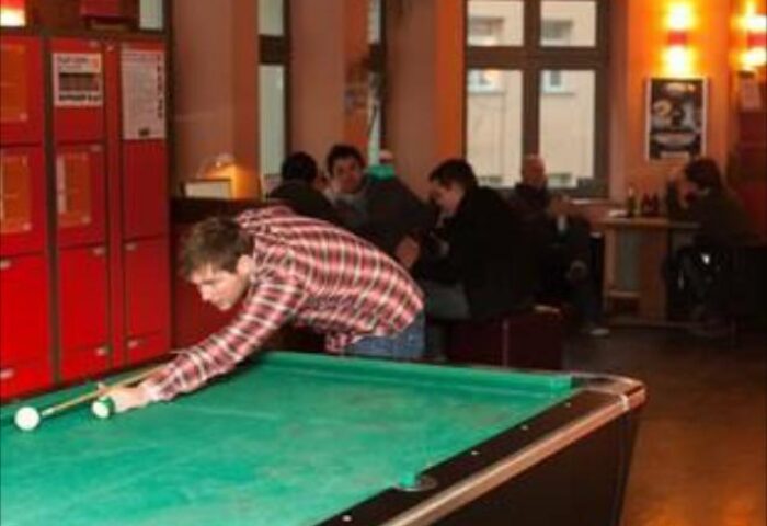 A man playing pool at St. Christopher's gay-friendly Hostel in Berlin. Travelers relax in the background of this Berlin hostel.