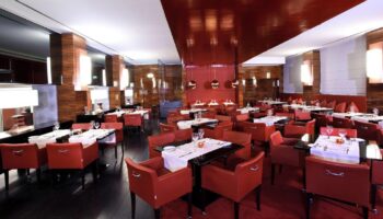 Starhotels Ritz, gay-friendly hotel restaurant. Elegant dining room with red chairs, dark tables, and wood accents. Upscale ambiance for gay travelers.