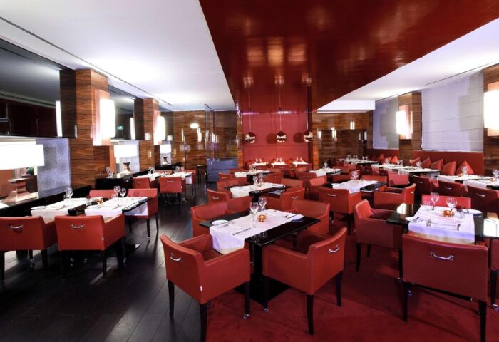 Starhotels Ritz, gay-friendly hotel restaurant. Elegant dining room with red chairs, dark tables, and wood accents. Upscale ambiance for gay travelers.